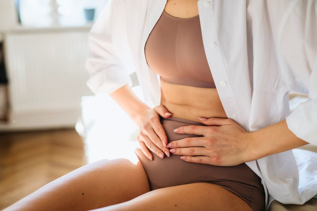 Une femme assise sur un sofa, souffrant de crampes et douleurs menstruelles au ventre