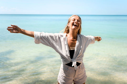 Femme souriante profitant du soleil sur une plage de sable fin avec un maillot de bain menstruel et d'une chemise