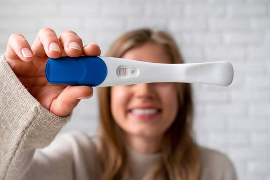 Femme souriante tenant un test de grossesse positif avec les deux lignes rouges