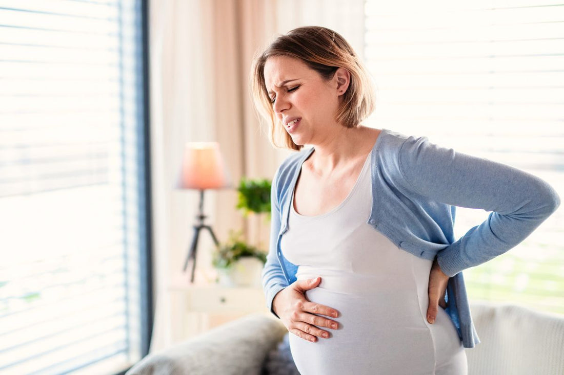 Femme enceinte avec une expression de souffrance tenant son ventre et son bas du dos souffrant de douleurs