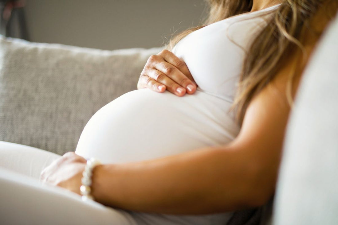 Close-up of a pregnant woman wearing a white outfit, her hands gently placed on her belly