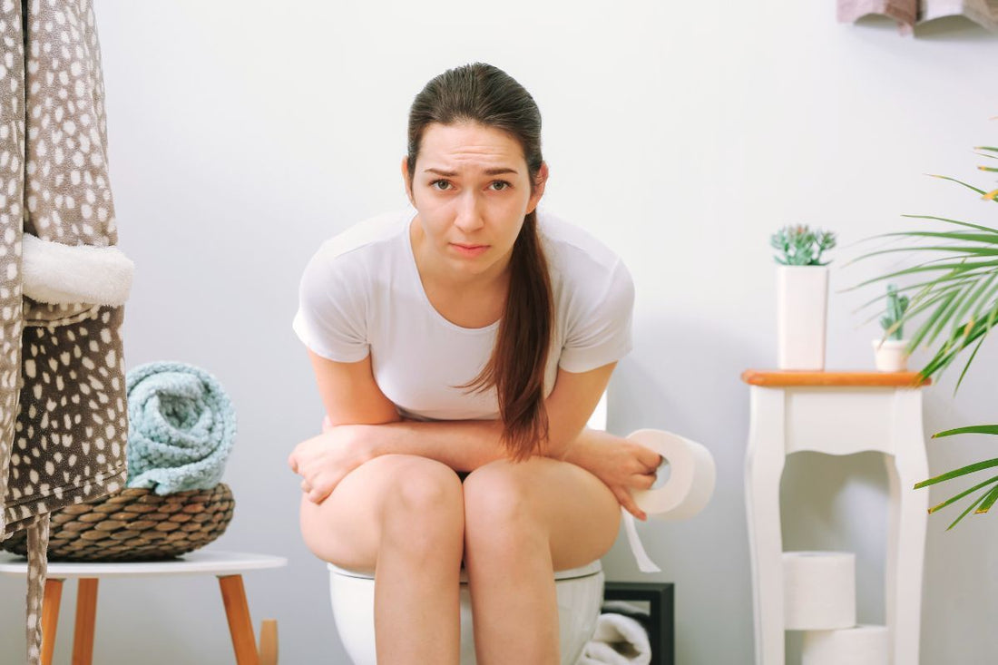 Une femme est assise sur les toilettes, exprimant une douleur ou une gêne urinaire aiguë pendant ses règles