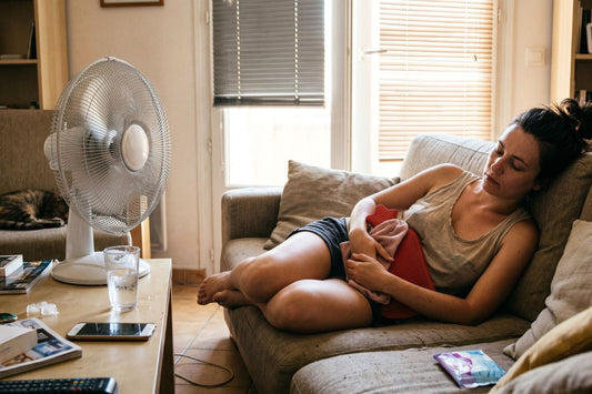 Femme allongée sur son canapé avec une bouillotte posée sur le ventre pendant une canicule