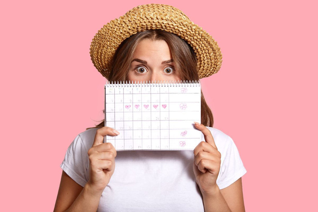 Jeune femme surprise cachant son visage derrière un calendrier menstruel annoté pour le suivi des règles et l'indication d'un possible retard de cycle