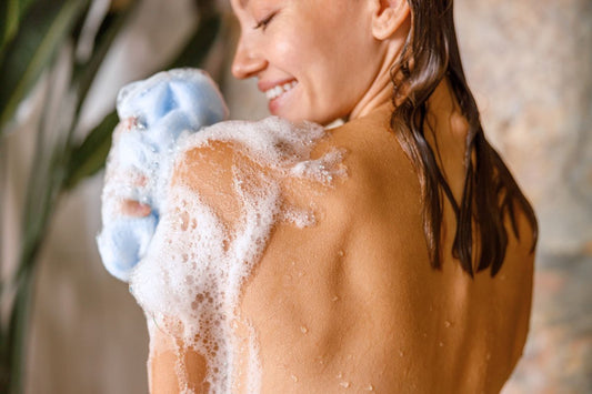 Femme souriante sous la douche utilisant une éponge pour routine d'hygiène corporelle et intime