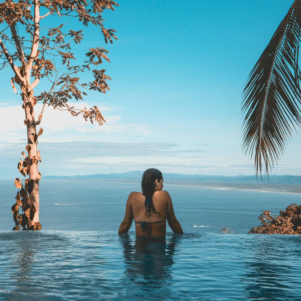 Femme de dos en maillot de bain menstruel regardant la mer depuis une piscine à débordement