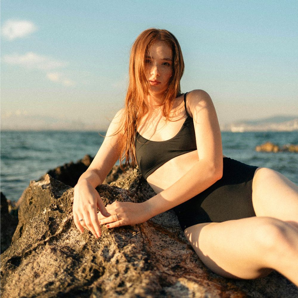 Jeune fille en maillot de bain menstruel posant sur des rochers en bord de mer